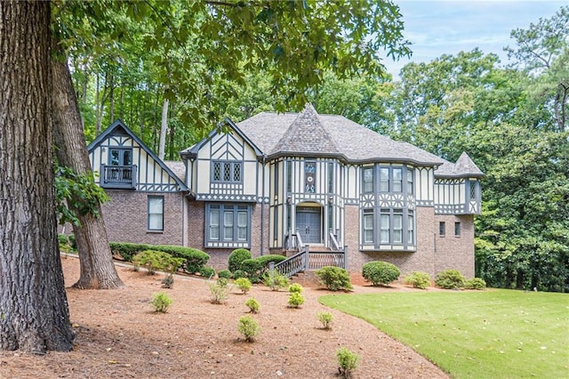 tudor home with brick siding, a front yard, and roof with shingles