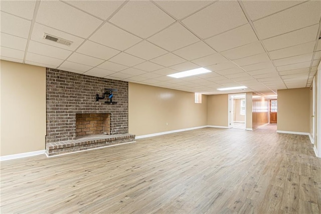 unfurnished living room featuring a paneled ceiling, visible vents, a brick fireplace, wood finished floors, and baseboards