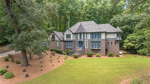 tudor home featuring brick siding, a balcony, and a front yard