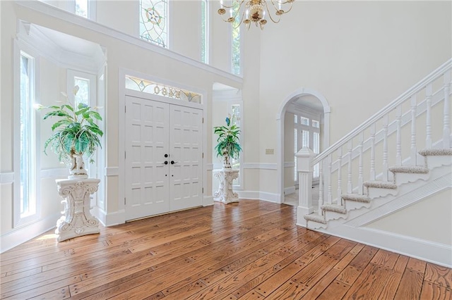 foyer with arched walkways, a chandelier, a high ceiling, stairs, and light wood-style flooring