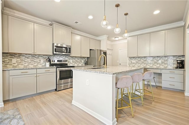 5322 Burrus Ln SW, Mableton, GA 30126 - kitchen featuring appliances with stainless steel finishes, backsplash, light wood-style flooring, a kitchen island with sink, and ornamental molding