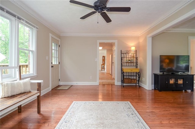 living area featuring light wood-type flooring, a ceiling fan, baseboards, and crown molding