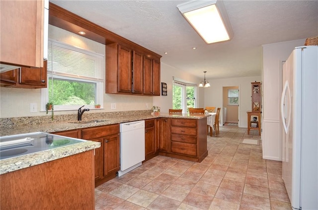 kitchen featuring brown cabinetry, a peninsula, white appliances, light stone counters, and a sink