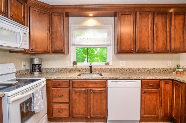 kitchen with brown cabinetry, white appliances, tasteful backsplash, light stone counters, and a sink