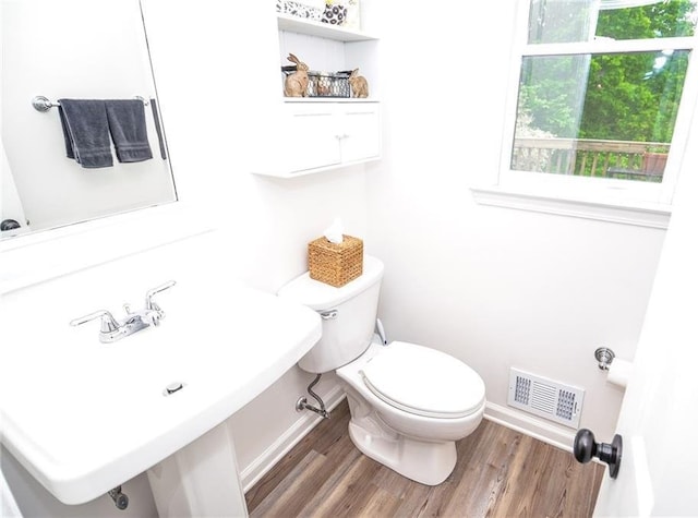 half bath with visible vents, wood finished floors, toilet, baseboards, and a sink