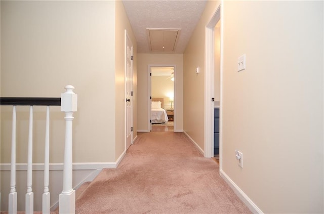 hallway with baseboards, attic access, light colored carpet, a textured ceiling, and an upstairs landing