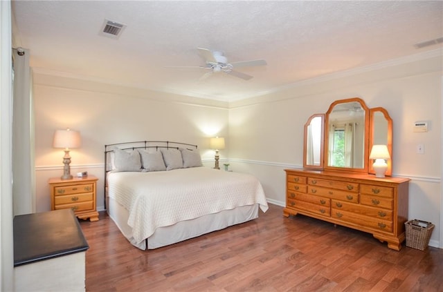 bedroom with ceiling fan, visible vents, ornamental molding, and wood finished floors