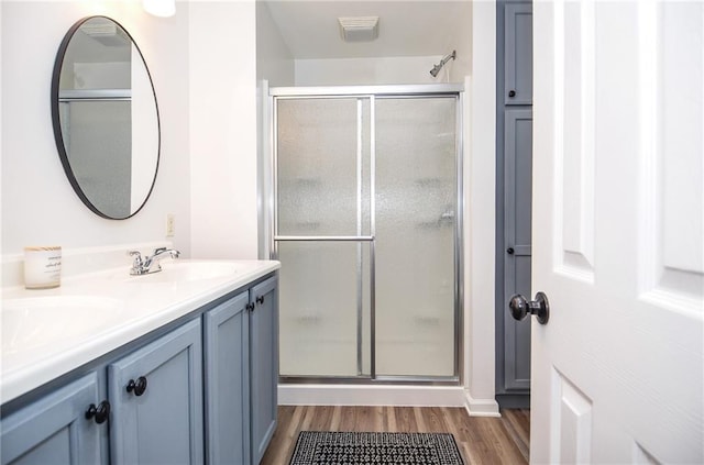 full bathroom with double vanity, visible vents, a stall shower, wood finished floors, and a sink