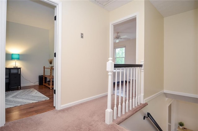 corridor featuring carpet floors, baseboards, wood finished floors, and an upstairs landing