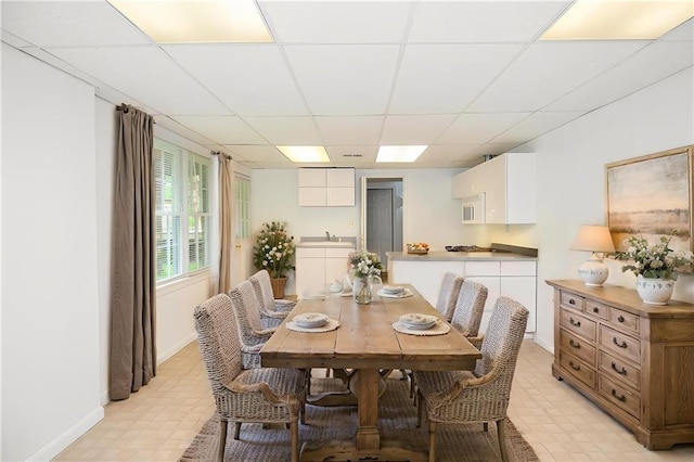 dining room featuring baseboards, light floors, and a drop ceiling