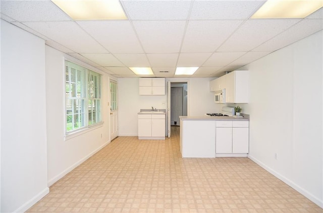 kitchen with white cabinets, white microwave, a peninsula, a drop ceiling, and light floors