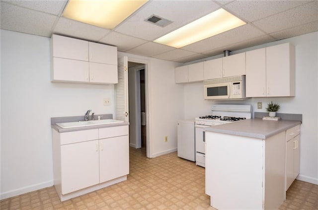 kitchen featuring a sink, light floors, a drop ceiling, and white appliances