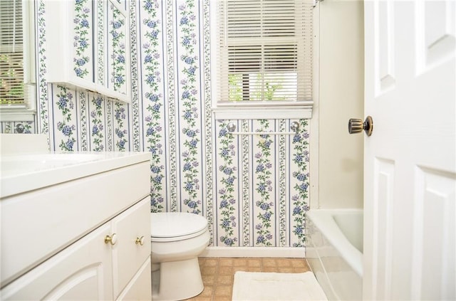 bathroom with vanity, toilet, baseboards, wallpapered walls, and a bath