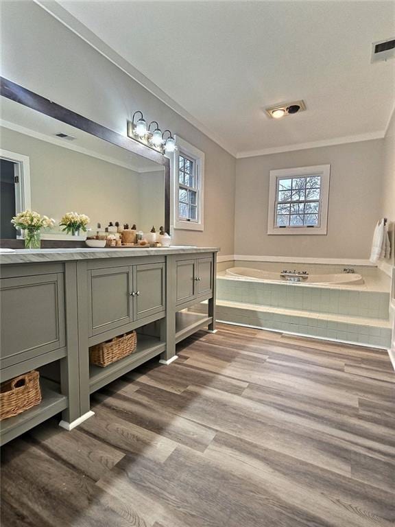 bathroom featuring vanity, wood-type flooring, crown molding, and tiled bath