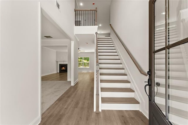 418 Brookstone Trl, Dawsonville, GA 30534 - staircase featuring a warm lit fireplace, wood finished floors, a towering ceiling, ceiling fan, and baseboards