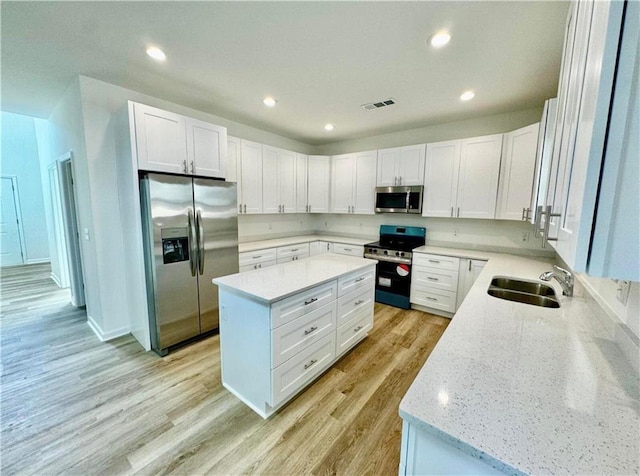 kitchen with sink, appliances with stainless steel finishes, white cabinetry, a center island, and light stone counters