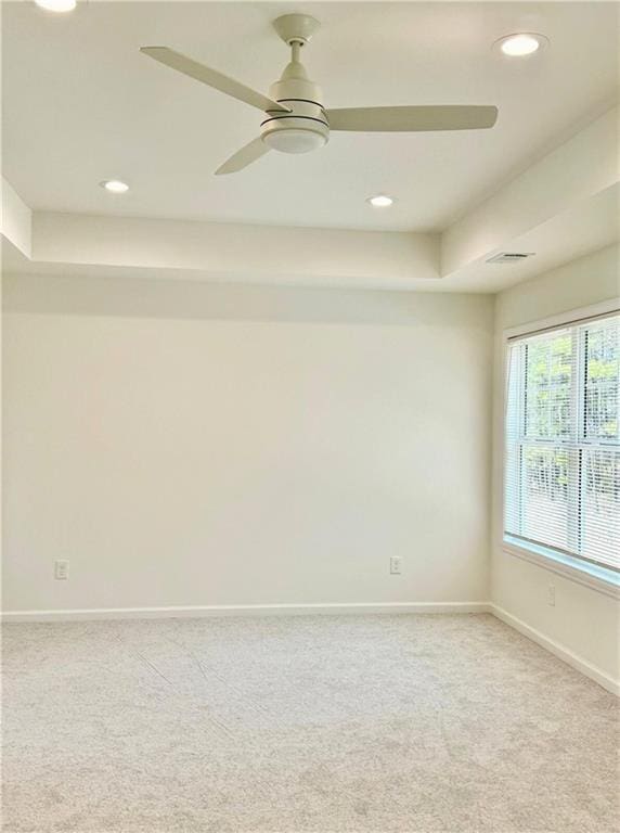 empty room featuring a raised ceiling, light carpet, and ceiling fan