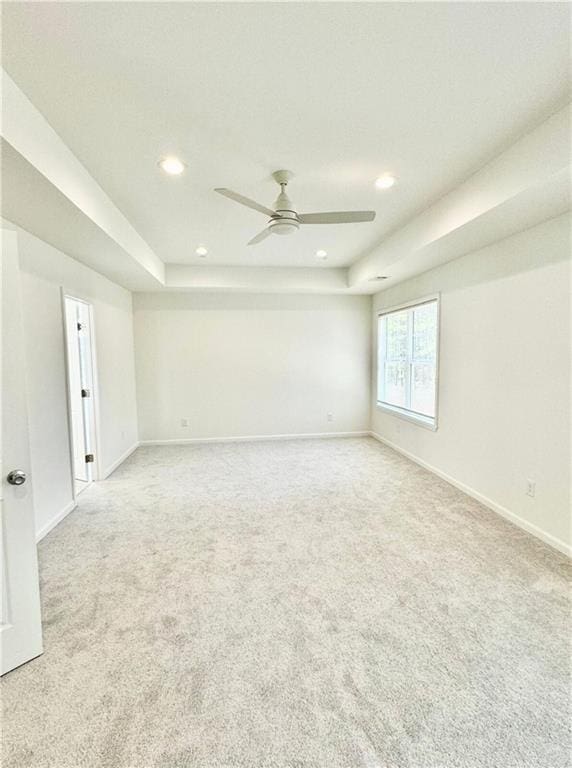 unfurnished room with light carpet, ceiling fan, and a tray ceiling