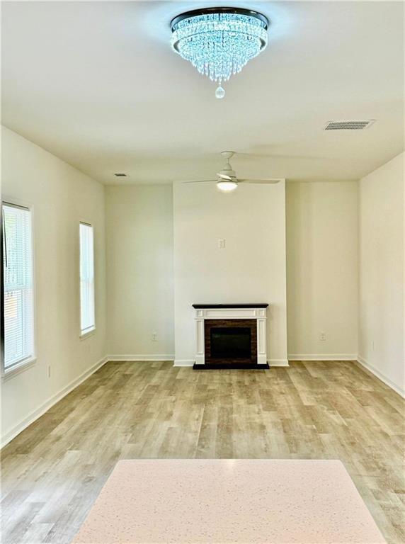 unfurnished living room featuring ceiling fan with notable chandelier, hardwood / wood-style floors, and a brick fireplace