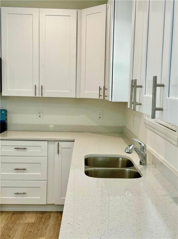 kitchen with light stone counters, light wood-type flooring, sink, and white cabinets