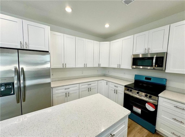 kitchen with white cabinetry, light stone counters, light hardwood / wood-style flooring, and appliances with stainless steel finishes