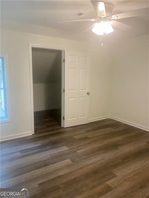 unfurnished bedroom with dark wood-style floors, baseboards, a spacious closet, a ceiling fan, and a closet