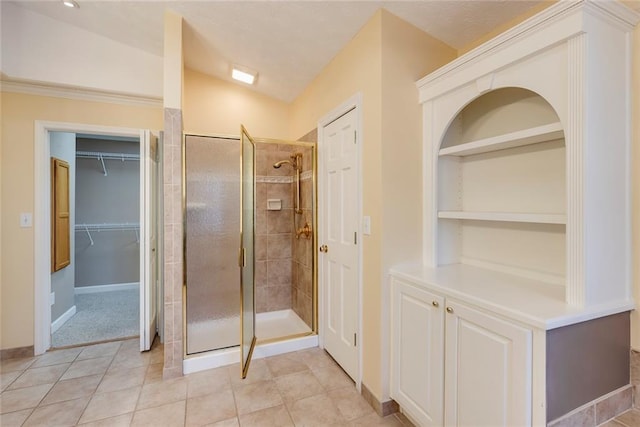 bathroom featuring tile patterned flooring, a shower stall, built in shelves, a walk in closet, and baseboards