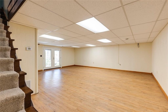 below grade area with light wood finished floors, visible vents, stairs, french doors, and a paneled ceiling