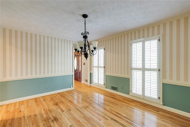 empty room with visible vents, wallpapered walls, an inviting chandelier, hardwood / wood-style flooring, and a textured ceiling