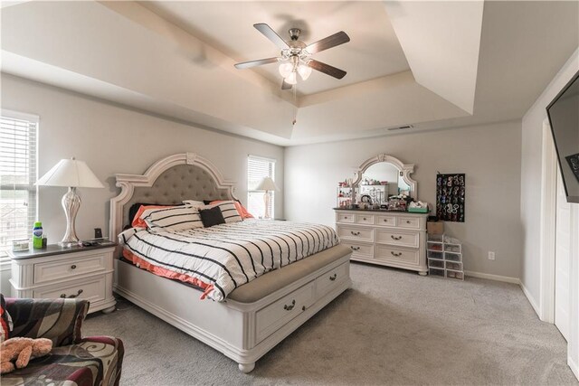 carpeted bedroom featuring ceiling fan, multiple windows, and a raised ceiling