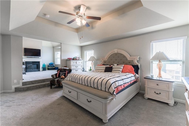 carpeted bedroom with ceiling fan and a tray ceiling