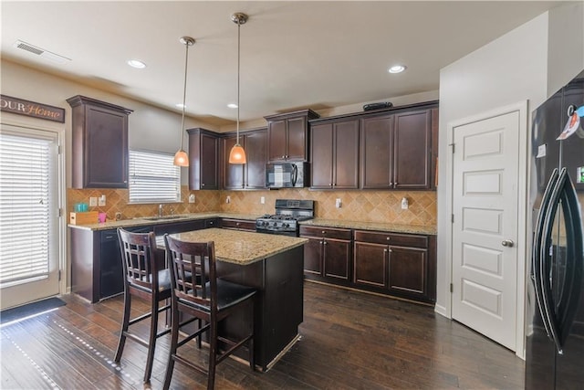 kitchen featuring pendant lighting, dark brown cabinetry, black appliances, a kitchen island, and a breakfast bar