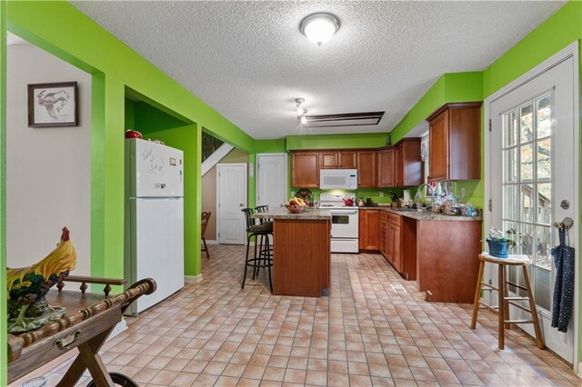 kitchen with a kitchen breakfast bar, a textured ceiling, sink, a center island, and white appliances