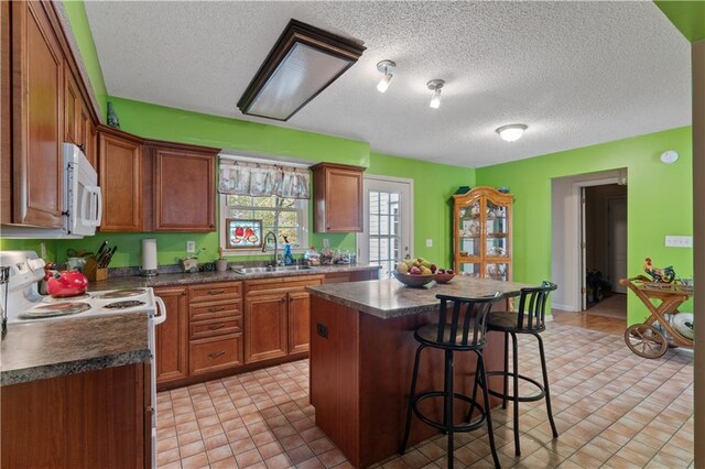 kitchen featuring a kitchen island, a textured ceiling, a kitchen bar, sink, and white appliances