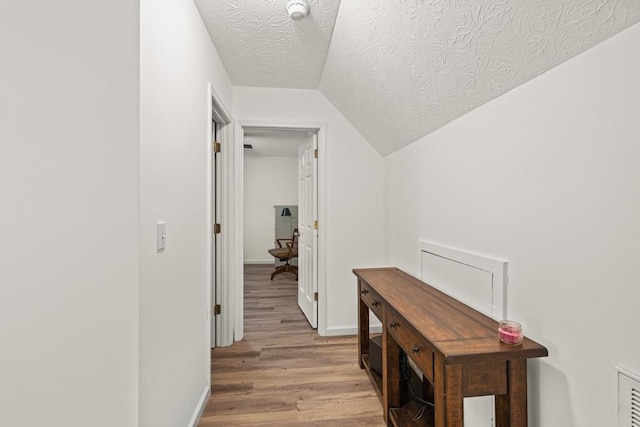 hall featuring lofted ceiling, light hardwood / wood-style floors, and a textured ceiling