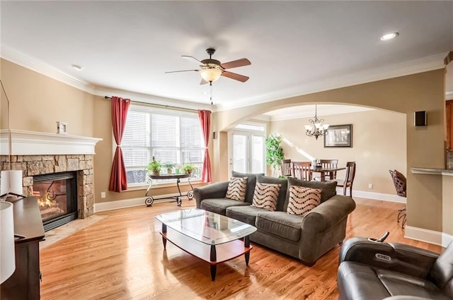 living room featuring a fireplace, ceiling fan with notable chandelier, ornamental molding, and light wood-type flooring