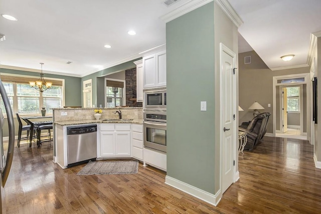 212 Westwind Dr, Newnan, GA 30263 - kitchen featuring appliances with stainless steel finishes, a peninsula, white cabinetry, tasteful backsplash, and ornamental molding