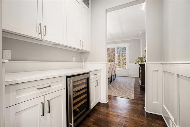 bar featuring dark wood finished floors, wainscoting, wine cooler, ornamental molding, and a bar