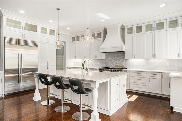 kitchen with tasteful backsplash, stainless steel built in fridge, premium range hood, and white cabinetry