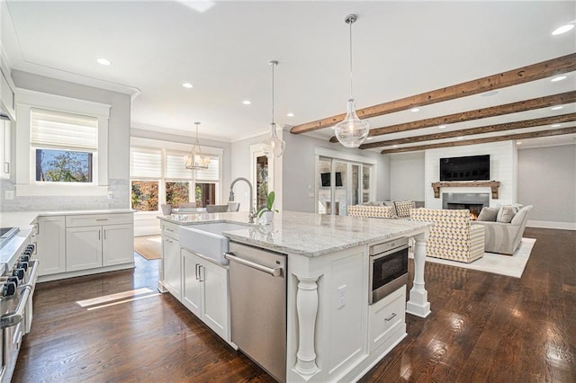 kitchen featuring a warm lit fireplace, light stone counters, stainless steel appliances, a sink, and dark wood-style floors