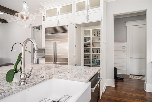 kitchen with light stone counters, built in fridge, a sink, white cabinets, and dark wood finished floors