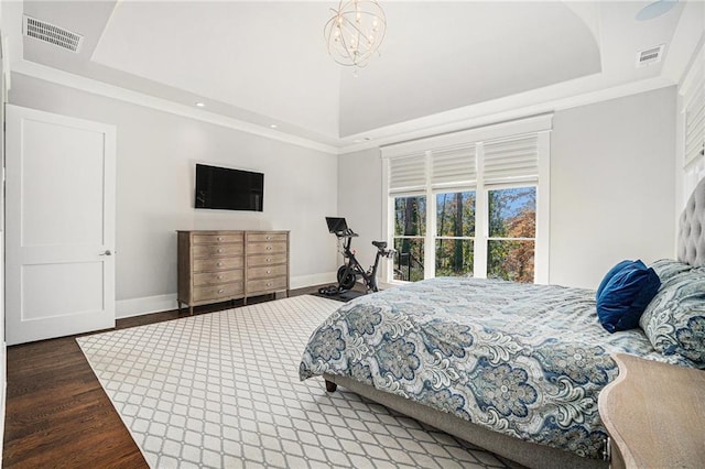 bedroom with a raised ceiling, visible vents, baseboards, and wood finished floors