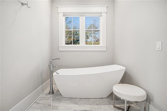 full bathroom featuring marble finish floor, a freestanding bath, and baseboards