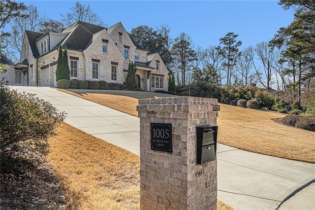 french provincial home featuring a garage, a front yard, stone siding, and concrete driveway