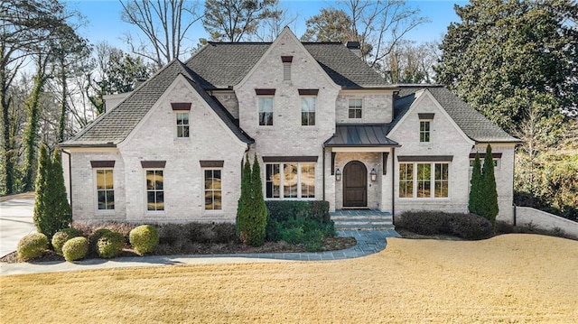 french country inspired facade with metal roof, brick siding, a standing seam roof, and a front yard