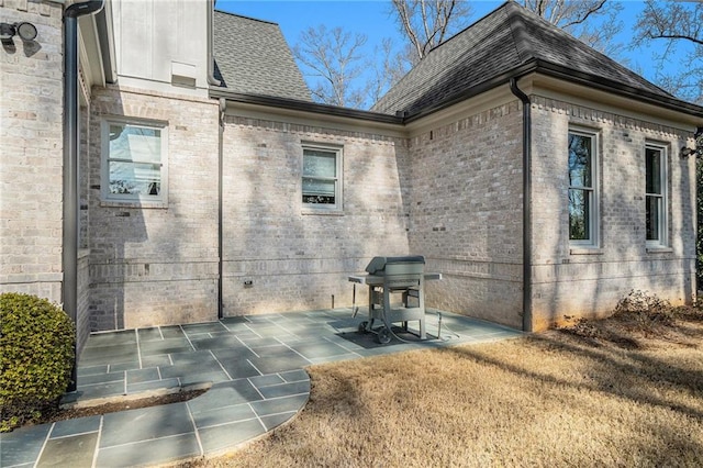 view of side of property with a shingled roof, a patio, and brick siding