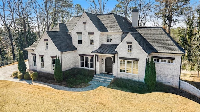 french provincial home featuring brick siding, a chimney, metal roof, a standing seam roof, and a front yard