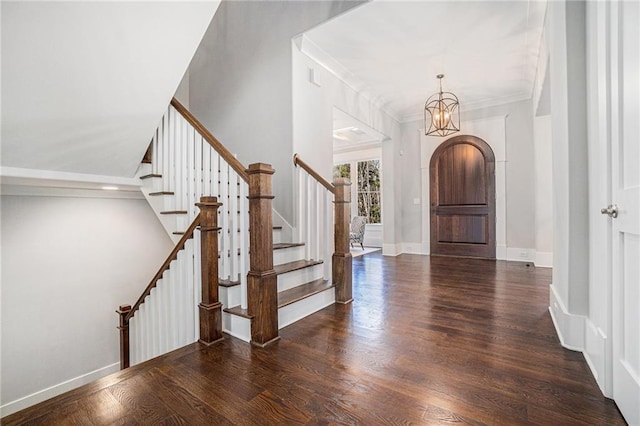 entrance foyer featuring arched walkways, wood finished floors, baseboards, stairs, and ornamental molding