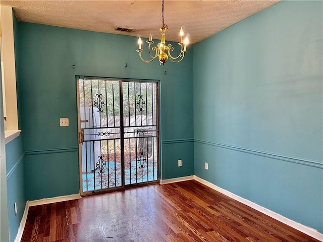 empty room with wood finished floors, a textured ceiling, visible vents, an inviting chandelier, and baseboards