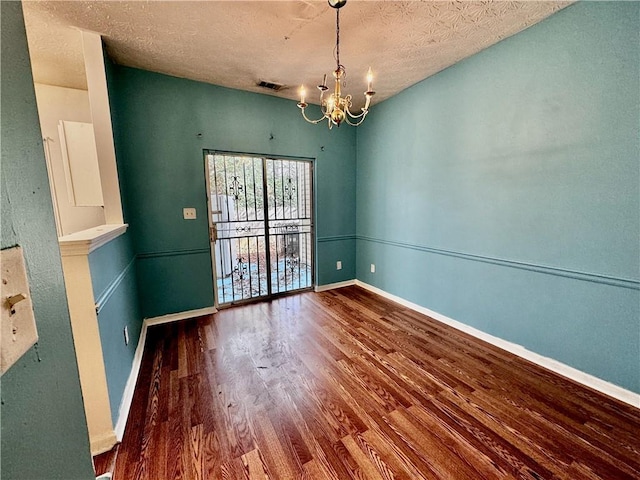 spare room with an inviting chandelier, wood finished floors, a textured ceiling, visible vents, and baseboards